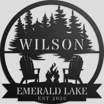 Custom campfire by the lake metal wall art sign in powder-coated matte black, featuring pine trees, chairs, and personalized text, mounted on a light gray studio wall.